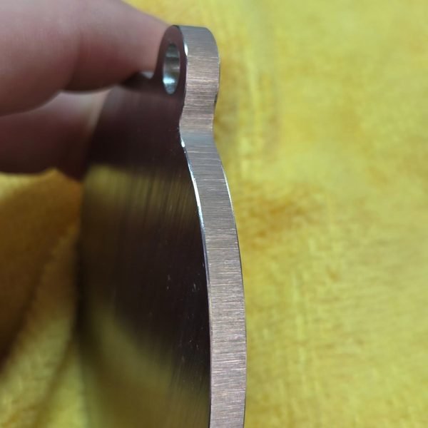 A blank steel medallion held up edge-on, showing the cut profile before engraving.
