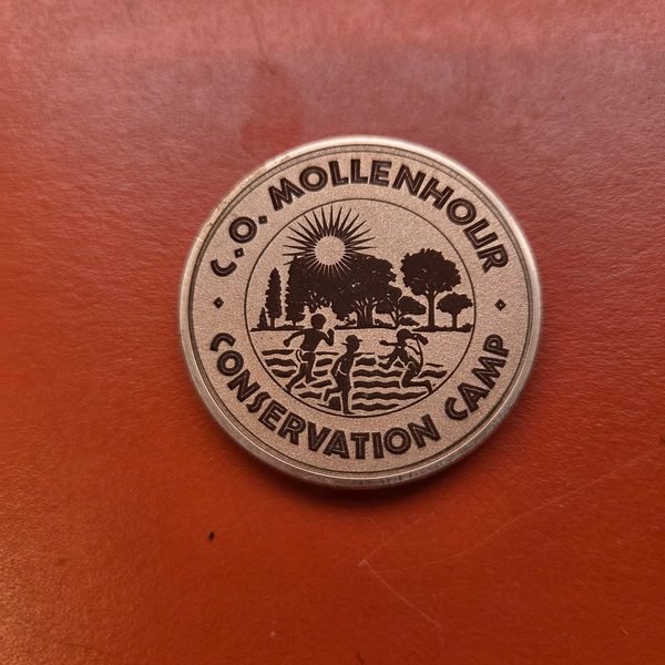 A copper coin fiber-engraved with the C.O. Mollenhour Conservation Camp emblem.