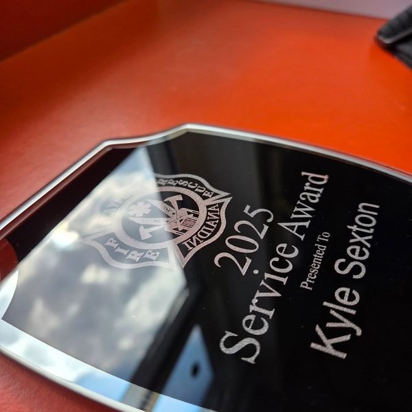 An angled close-up of a mirrored service award, the engraved crest and lettering catching the reflection.