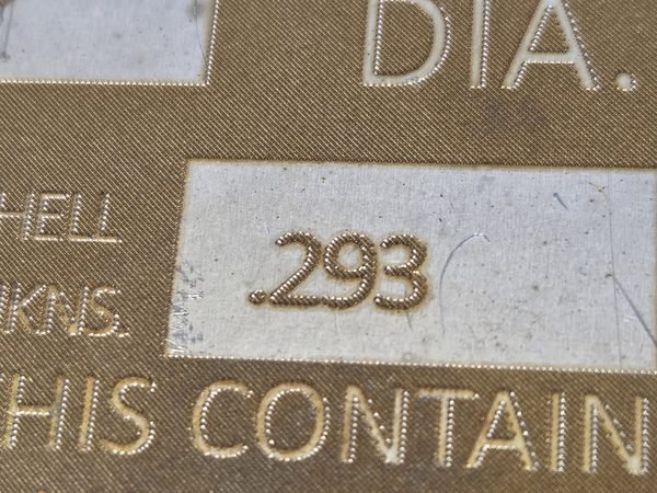 A macro view of an engraved brass data plate, the cut edges of the lettering catching the light.