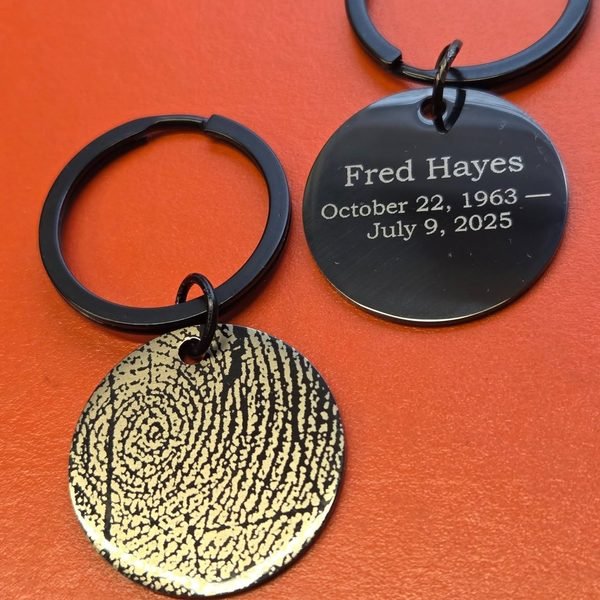 A memorial keyring pairing an engraved black name tag with a gold disc carrying a fingerprint.