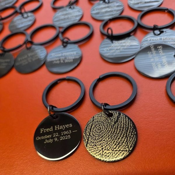 A group of memorial keyrings, black name tags and gold fingerprint discs laid out together.