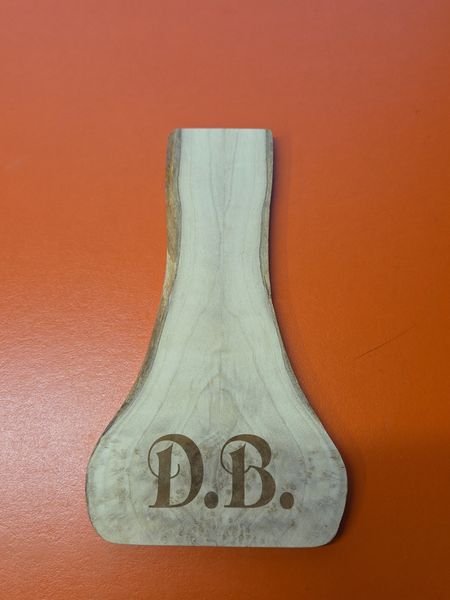 A live-edge wooden paddle engraved with the monogram D.B. in serif capitals.