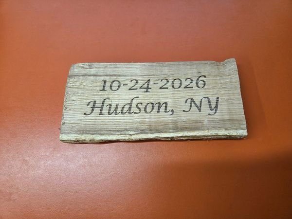 A block of weathered barn wood engraved 10-24-2026, Hudson, NY.