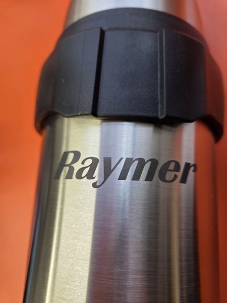 A close-up of a brushed steel travel mug engraved with the name Raymer in bold italics.