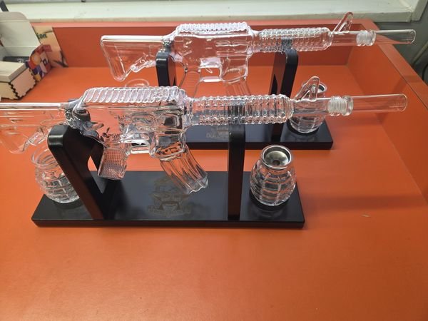 Two rifle-shaped glass decanters on engraved black stands, each with matching grenade-shaped glasses.
