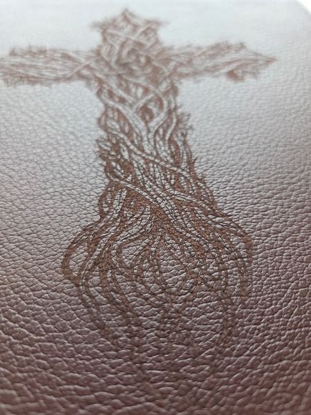 A macro view of the thorn-branch cross engraved into the leather Bible cover, the grain of the hide showing through.