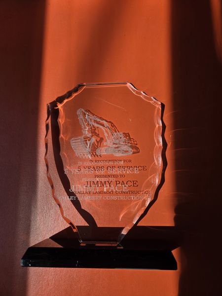 The engraved excavator award lit from the side, the frosted marks catching the light against its chiselled edges.