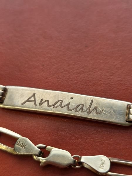 A close-up of the gold bracelet plate, the name Anaiah engraved in fine script across the brushed surface.