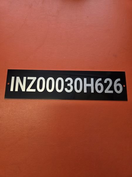 A black metal identification plate engraved through to bright metal with a serial number.