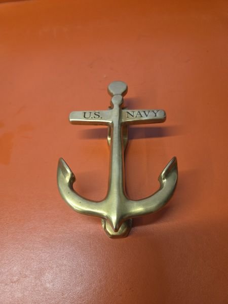 A solid brass anchor door knocker engraved U.S. Navy across its stock in black serif capitals.