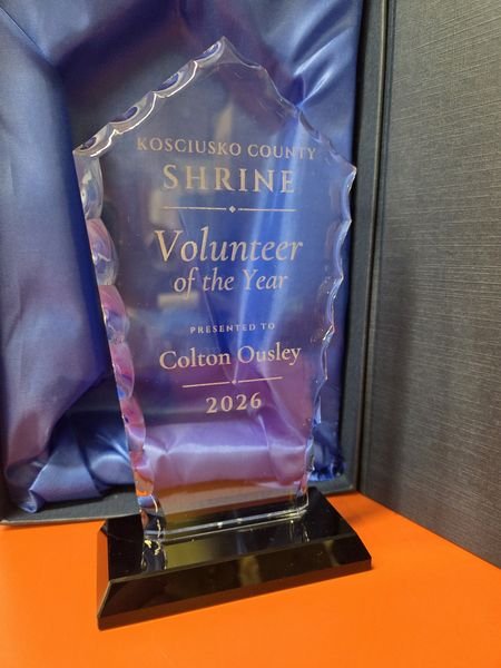 The Volunteer of the Year crystal standing in front of its open box, the etched lettering glowing against the blue satin.