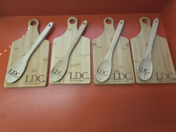 Four bamboo paddle boards laid out with a matching spoon on each, every piece engraved with the LDC Louis Dreyfus Company logo.