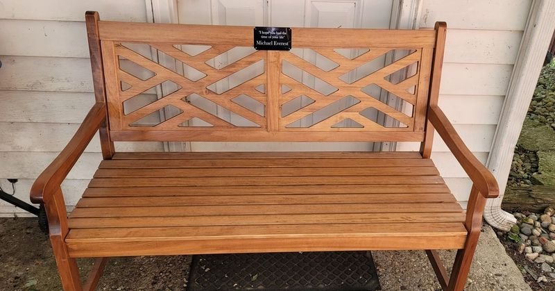 A wooden garden bench with the black memorial plaque fixed to the centre of its top rail.