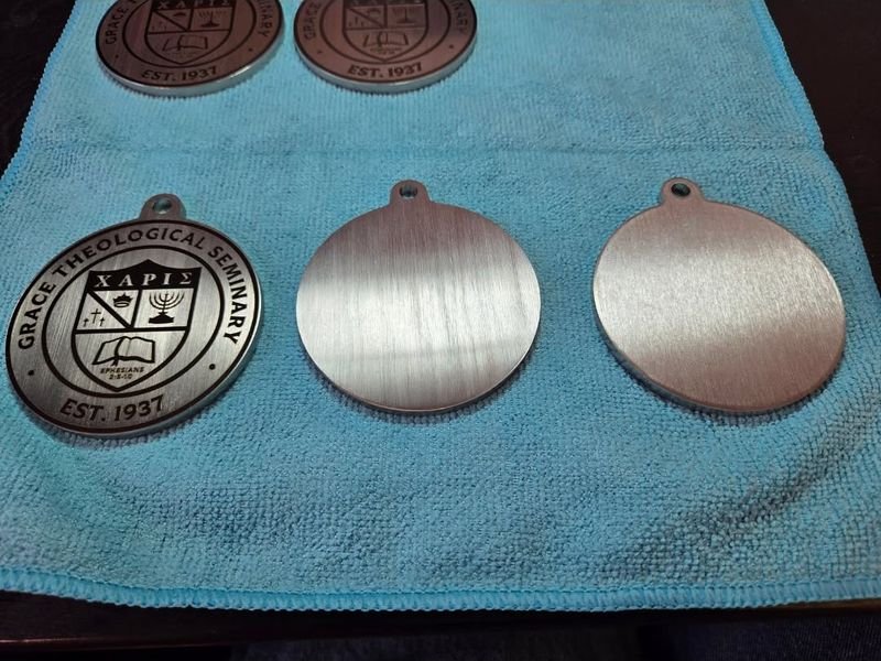 Three matching metal discs side by side — the engraved crest, a polished blank, and a rough one.