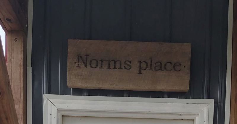 The engraved board mounted on dark siding above a white-framed cabin door.