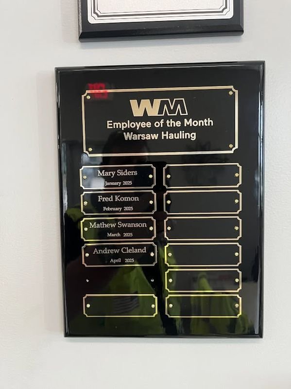 The black Employee of the Month plaque on a wall, with four name plates fitted and empty slots below.